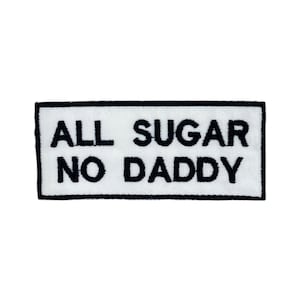 May include: A rectangular white patch with black embroidered text that reads "ALL SUGAR NO DADDY". The patch has a black border and is likely designed to be sewn or ironed onto clothing or accessories.