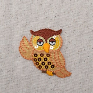 May include: A brown and orange owl applique with sequins for eyes and a brown felt body. The owl is embroidered with brown thread and has a light orange felt wing.