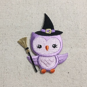 Puede incluir: Búho bordado de color morado con un sombrero de bruja negro con una hebilla dorada y sosteniendo una escoba dorada y marrón.