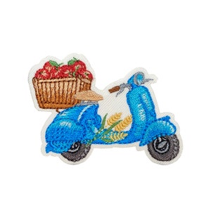 May include: Embroidered patch of a blue scooter carrying a basket of red strawberries. The scooter has a wheat stalk behind it.