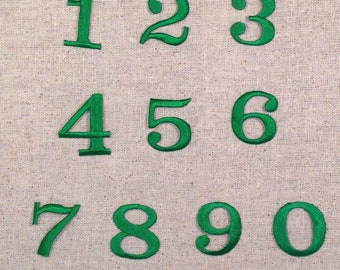 May include: Green embroidered numbers 1 through 0 on a beige fabric background.