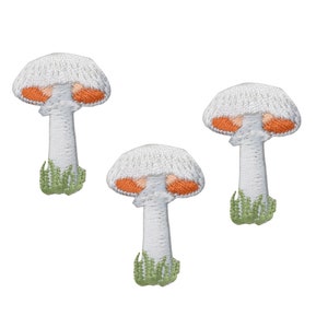 May include: Three white embroidered mushroom patches with orange accents. Each mushroom has a white stem and green grass at the base.