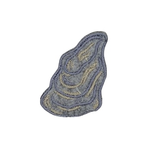 May include: A gray embroidered patch with a unique, organic shape. The patch features a layered design with light gray and beige thread, creating a textured appearance. The patch is likely for clothing or accessories.