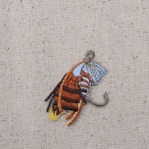 Puede incluir: Parche de mariposa bordada con detalles marrones, azules y amarillos. El parche presenta costuras intrincadas y un diseño detallado, perfecto para agregar a la ropa o los accesorios. La mariposa tiene una antena curva y está sobre un fondo neutro.