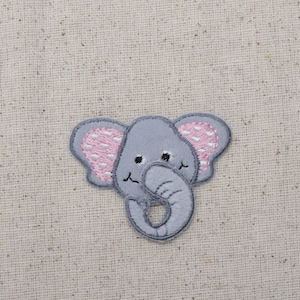 May include: A gray embroidered elephant with pink polka dot ears. The elephant is holding its trunk with its right hand.
