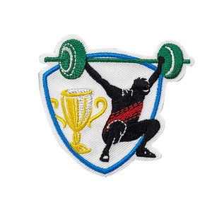 May include: An embroidered patch with a blue, yellow, and white shield. Inside the shield is a black silhouette of a weightlifter lifting a barbell with green weights. A gold trophy is in the lower left corner of the shield.