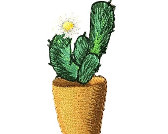 Puede incluir: Una planta de cactus verde con una flor blanca florece en una maceta marrón. El cactus está bordado con hilo verde y la maceta está bordada con hilo marrón.