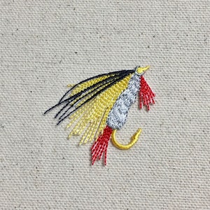 Puede incluir: Primer plano de un señuelo de pesca negro, amarillo y rojo con un anzuelo plateado.