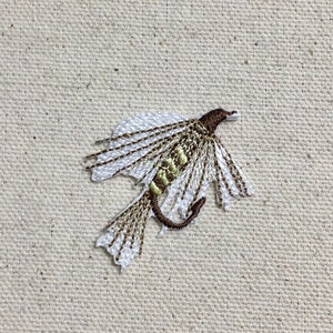 Puede incluir: Una mosca de pesca con mosca bordada de color marrón y blanco con un cuerpo verde y alas marrones.