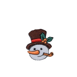 May include: A brown and white snowman face with a red and brown top hat, green holly leaves, and a carrot nose. The snowman is holding a brown pipe in its mouth.