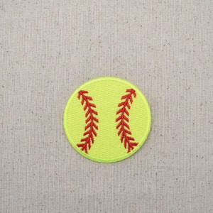 May include: A yellow softball with red stitching. The softball is on a beige fabric background.