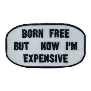 Op de afbeelding: Geborduurde patch met de tekst "BORN FREE BUT NOW I'M EXPENSIVE" in zwarte blokletters op een witte ovale achtergrond met een zwarte rand. De patch is waarschijnlijk voor kleding of accessoires.