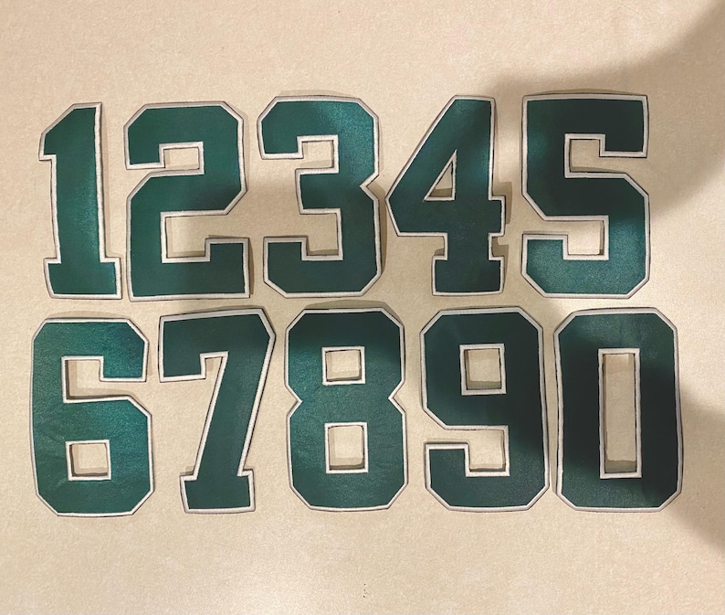 May include: Ten green felt patches with white outlines, each featuring a number from 1 to 10. The numbers are in a bold, blocky font.