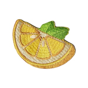 Op de afbeelding: Geborduurde patch in de vorm van een citroenpartje met een groen blad. De citroenpartje is geel met witte en oranje accenten, en het blad is groen. De patch is waarschijnlijk voor kleding of accessoires.