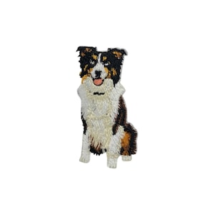 Könnte beinhalten: Gestickter Aufnäher eines sitzenden Hundes. Der Hund hat ein dreifarbiges Design mit einem schwarzen und braunen Kopf, einer weißen Brust und braunen und beigen Markierungen. Der Aufnäher zeigt eine rosa Zunge und detaillierte Nähte.