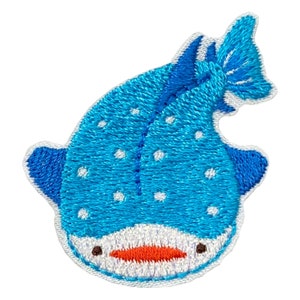 May include: A blue and white embroidered patch of a whale shark with a white belly and a small orange mouth.