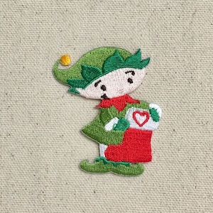 May include: Green and red embroidered Christmas elf holding a stocking with a red heart on it.