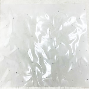 May include: A sheer, white fabric with scattered, small, silver-colored rhinestones. The fabric is slightly wrinkled, creating shadows and highlights. The overall effect is delicate and shimmering, suggesting a decorative or craft material.