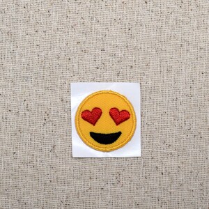 May include: Yellow embroidered iron-on patch with a smiley face with red heart eyes.
