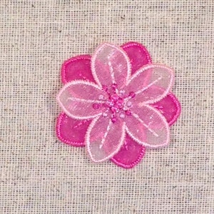 May include: A pink and white layered flower embellishment with a beaded center. The flower is made of sheer fabric and has a delicate, feminine look.
