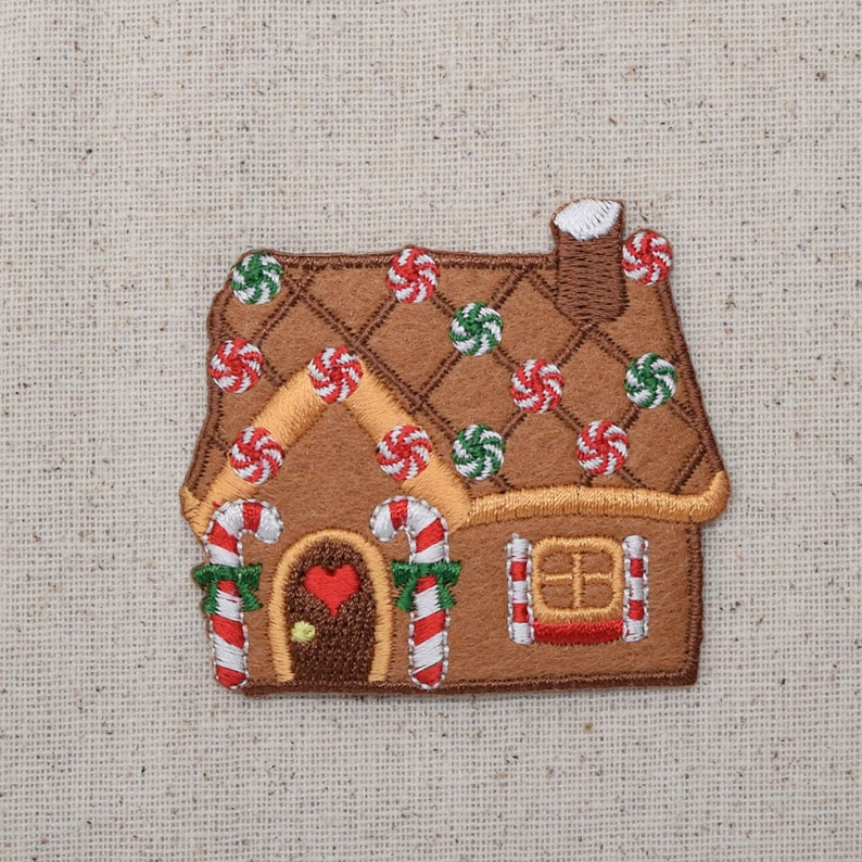 May include: A gingerbread house patch with a brown roof decorated with white and green candy swirls. The house has a red heart-shaped door and white candy cane trim.
