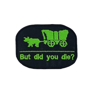 May include: Black embroidered patch with a green covered wagon and oxen design. The text "But did you die?" is embroidered in green below the wagon. The patch has a black border.