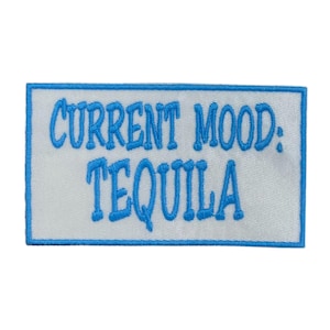 May include: A rectangular patch with a white background and a light blue border. The text "CURRENT MOOD: TEQUILA" is embroidered in light blue, centered on the patch. The patch is likely designed to be sewn or ironed onto clothing or accessories.