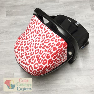 May include: Red and white leopard print car seat canopy. The canopy is made of a soft, stretchy fabric and fits snugly over the car seat. The canopy is designed to protect the baby from the sun and wind.