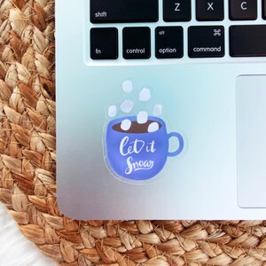 May include: A blue and white sticker with a mug of hot chocolate and marshmallows. The text on the sticker says "Let it Snow".