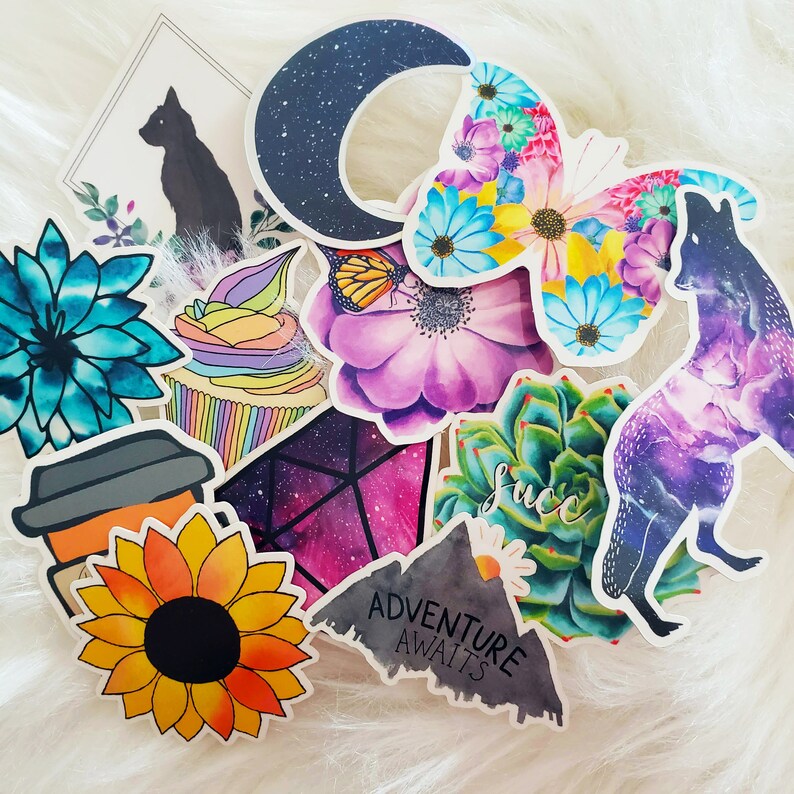 May include: A collection of colorful stickers featuring various designs, including a crescent moon, a butterfly, a succulent, a coffee cup, a cupcake, a geometric pattern, and a galaxy-themed design. The stickers have a variety of colors, including purple, blue, green, pink, and yellow.