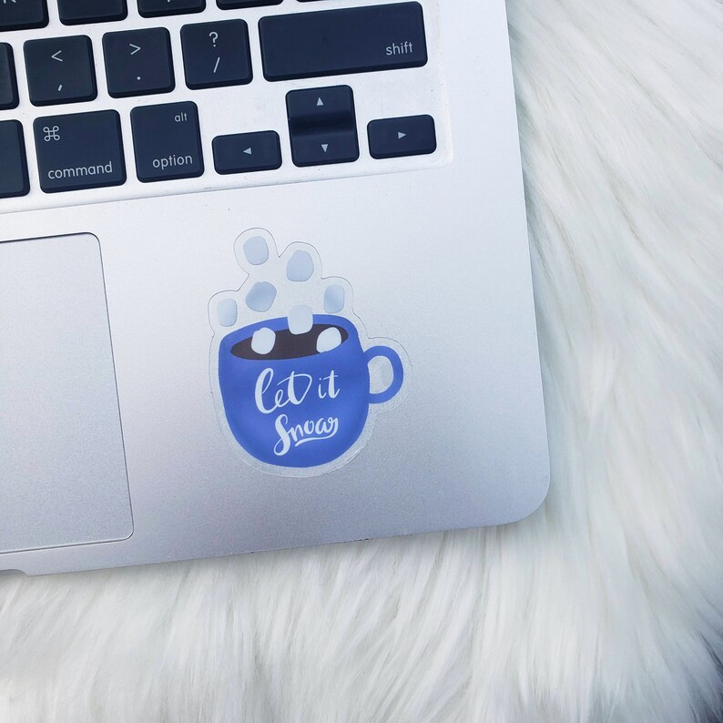 May include: A blue mug with white marshmallows and steam coming out of it. The mug has the text "Let it Snow" written on it.