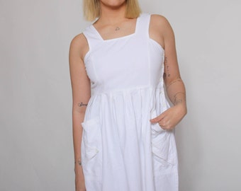 May include: A white sleeveless maxi dress with a square neckline and two large pockets on the front. The dress has a gathered skirt and a button closure on the side.