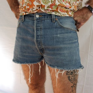 Puede incluir: Un par de pantalones cortos de mezclilla azul con bordes deshilachados. Los pantalones cortos tienen cierre de botón y cinco bolsillos.