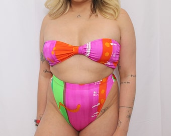 May include: A pink and orange patterned bikini top and high-waisted bikini bottom. The bikini top is strapless and the bikini bottom has a high cut leg.
