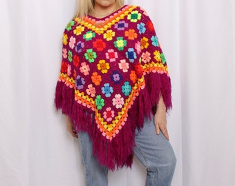 May include: A colorful crochet poncho with a fringe border. The poncho is made with a variety of bright colors, including pink, orange, yellow, green, blue, and purple. The poncho is a triangular shape and has a wide neckline.