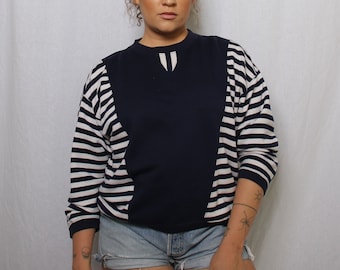 May include: A navy blue and white striped long-sleeve sweatshirt with a contrasting navy blue panel in the front. The sweatshirt has a round neckline and a relaxed fit.