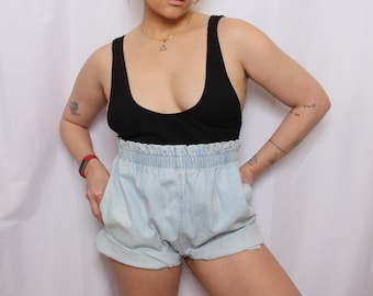 May include: A person wearing a black tank top, light blue denim shorts, and a green baseball cap with the text "Miller Genuine Draft" on the front.
