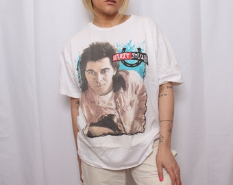 May include: White t-shirt with a graphic print of Marty Stuart, a country music singer. The graphic is in black, white, red, and blue. The text "Marty Stuart" is printed in red.