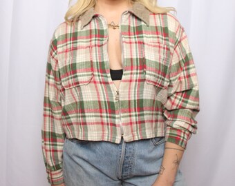 May include: A cropped plaid flannel shirt with a zipper closure. The shirt is red, green, and white with a brown collar.