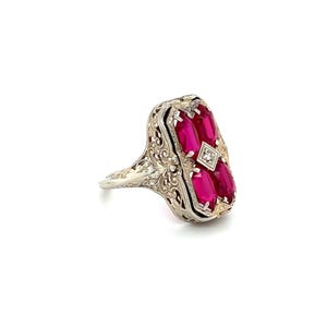 May include: An antique silver ring featuring a rectangular design with five oval-cut, vibrant red gemstones. A small, square diamond is set in the center. The ring has intricate filigree detailing.