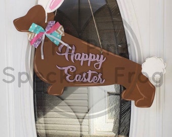 May include: A brown wooden dachshund shaped door hanger with bunny ears, a bow, and the text "Happy Easter".