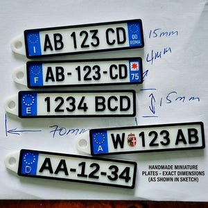 Op de afbeelding: Miniatuur kentekenplaten met zwarte randen en witte achtergronden. Elke plaat heeft een unieke alfanumerieke combinatie, met landcodes en een EU-embleem. De tekst "HANDMADE MINIATURE PLATES - EXACT DIMENSIONS (AS SHOWN IN SKETCH)" is ook zichtbaar.