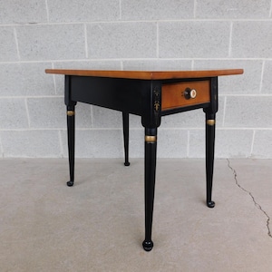 May include: A black end table with a single drawer and gold accents. The table has a wood top and black painted legs.