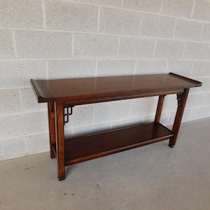 May include: A dark wood console table with a single shelf. The table has a simple, elegant design with intricate details on the legs.