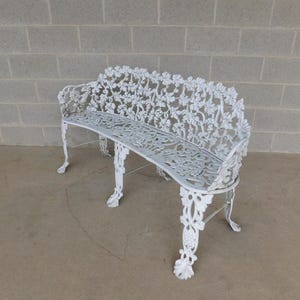 May include: White cast iron garden bench with intricate floral and leaf patterns. The bench has a curved seat and back, and ornate legs. The bench is approximately 48 inches long.