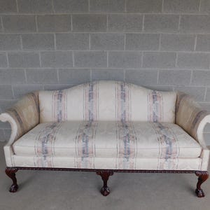 May include: A cream-colored loveseat with a curved back and rolled arms. The upholstery features vertical stripes in shades of blue, pink, and beige. The wooden frame has ornate, dark brown legs.