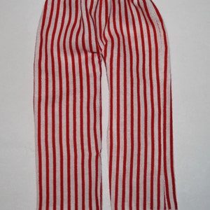 May include: Red and white striped pants. The pants have a vertical stripe pattern and an elastic waistband. The fabric appears to be a lightweight material. The pants are folded and laid flat on a white surface.