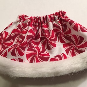 May include: A festive skirt with a red and white peppermint swirl pattern. The skirt has a white faux fur trim along the bottom edge and an elastic waistband. This holiday-themed skirt is perfect for seasonal celebrations.