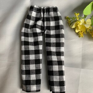 May include: Black and white checkered pants with an elastic waistband. The miniature pants are made of fabric and are designed for a doll or similar toy. The pants are displayed on a white surface.