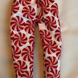 May include: White pants with a repeating pattern of red and white pinwheel designs. The pants have a drawstring waist and are made of a lightweight fabric. The overall theme is festive and playful.